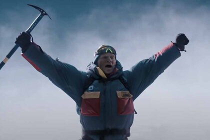 A bundled up mountain climber raises his arms with a pickaxe in one hand in Everest (2015).