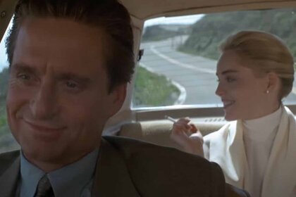Detective Nick Curran (Michael Douglas) smiles in the front seat of a car as Catherine Tramell (Sharon Stone) smiles in the back seat in Basic Instinct (1992).