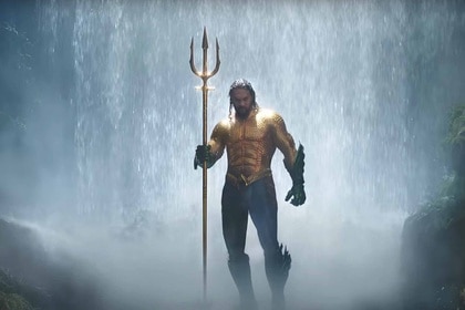 Aquaman (Jason Momoa) emerges from a waterfall holding a golden trident in Aquaman (2018).