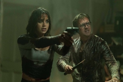 Joey (Melissa Barrera) points a gun next to Frank (Dan Stevens) in Abigail (2024).