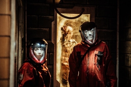 Murphy (Keith Allen) walks through a doorway in an orange Hazmat suit in Z Nation Episode 411.