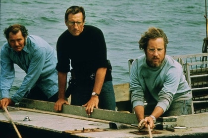 Quint (Robert Shaw), Martin Brody (Roy Scheider), and Matt Hooper (Richard Dreyfuss) pull on ropes and look out from a boat in Jaws (1975).