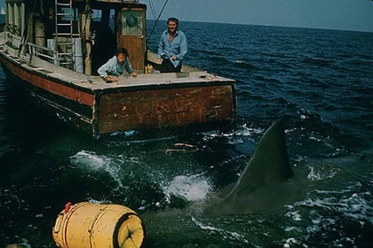 A giant shark fin appears near a boat and yellow buoy in Jaws (1975).