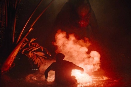 A D-Rex is illuminated by a flare in a man's hand in Jurassic World Rebirth (2025).