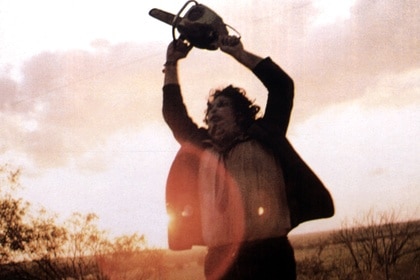 Leatherface (Gunnar Hansen) holds a chainsaw above his head in The Texas Chain Saw Massacre (1974).