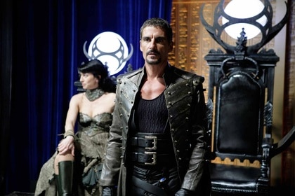 Vala Mal Doran (Claudia Black) sits in a thrne as Ba'al (Cliff Simon) stands in Stargate: Continuum (2008).