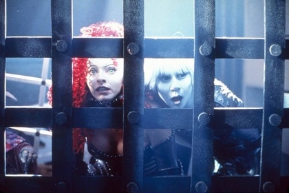 Jool (Tammy Macintosh) and Chiana (Gigi Edgley) look through a large metal grate in Farscape.