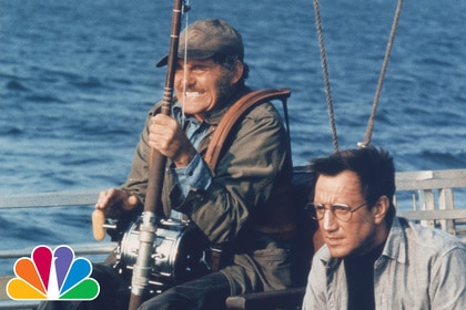 Robert Shaw reels in fishing rod as Roy Schieder stands beside him on boat in Steven Spielberg's Jaws (1975).