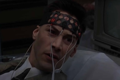 Johnny (Keanu Reeves) appears angry while strapped into a machine attached to his head.