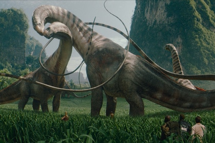 Titanosauruses groom each other as three humans ewatch in the bottom right corner in Jurassic World Rebirth (2025).