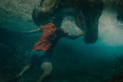 A T-Rex bites into water where a man is swimming in Jurassic World Rebirth (2025).