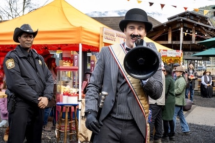 Sheriff Mike Thompson (Corey Reynolds) watches a costumed Mayor Ben Hawthorne (Levi Fiehler) speak on a megaphone on Resident Alien Episode 408.
