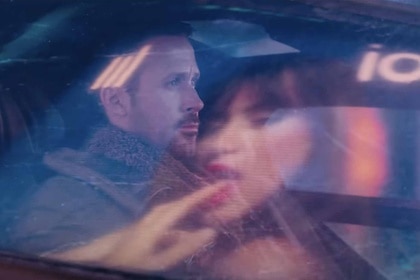 Officer K (Ryan Gosling) rides in a car as a reflection of a woman advertisement shines on the window in Blade Runner 2049 (2017).