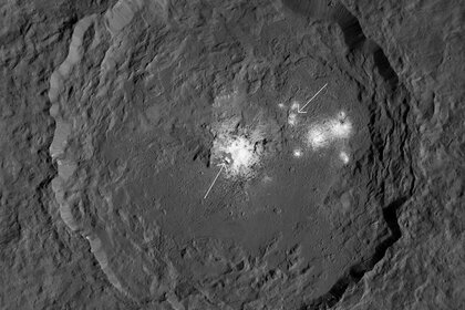Occator crater, a 92-kilometer-wide impact feature on Ceres, is covered in mineral deposits dredged up from the interior. Cerealia Facula is arrowed (left) as well as Vinalia Faculae (right). Credit: NASA/JPL-Caltech/UCLA/MPS/DLR/IDA/PSI / Phil Plait