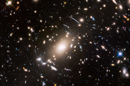 The galaxy cluster S1063 is a collection of hundreds of galaxies and is strewn with dark matter. This acts as a gravitational lens, distorting the light form more distant galaxies into arcs, which you can see throughout the center of this Hubble image. 