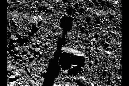 Moments before sample collection, the OSIRIS-REx boom and sample collector shadow stretched across the surface of the asteroid Bennu. Most of those rocks are a few centimeters across. Credit: NASA/Goddard/University of Arizona/Lockheed Martin