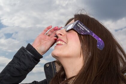 a woman uses safe glasses to view an eclipse