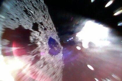 An image caught mid-bounce of the MINERVAII-1 A rover showing the surface of the asteroid Ryugu (left) and a reflection of sunlight (right).  Credit: JAXA