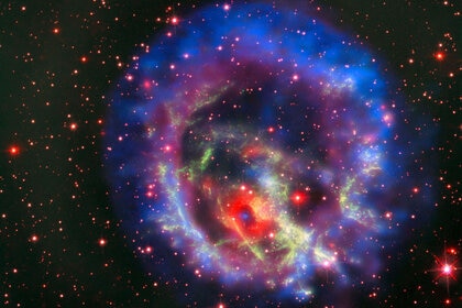 The supernova remnant 1E 0102.2-7219 seen by three telescopes: The red background (note the stars) from Hubble, the Very Large Telescope in green, and X-rays seen by Chandra X-ray Observatory in blue and purple.
