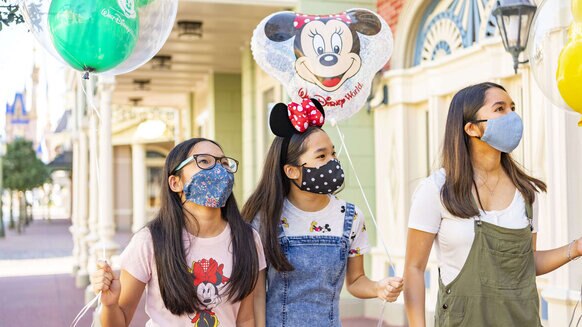 Three guests holding Disney balloons walking down Main Street, USA at Disney's Magic Kingdom