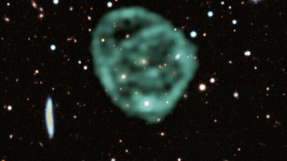 ORC1 in radio waves (green) superposed on visible light data from the Dark Energy Survey. The galaxy in the center can be seen as a yellowish dot.