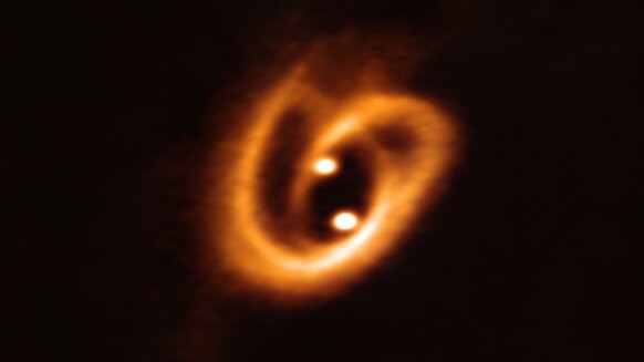 The two stars of the binary system [BHB2007] 11 are in the process of forming, drawing material from the disk surrounding both via a pair of filaments, wound up due to the motion of the stars around each other. Credit: ALMA (ESO/NAOJ/NRAO), Alves et al.