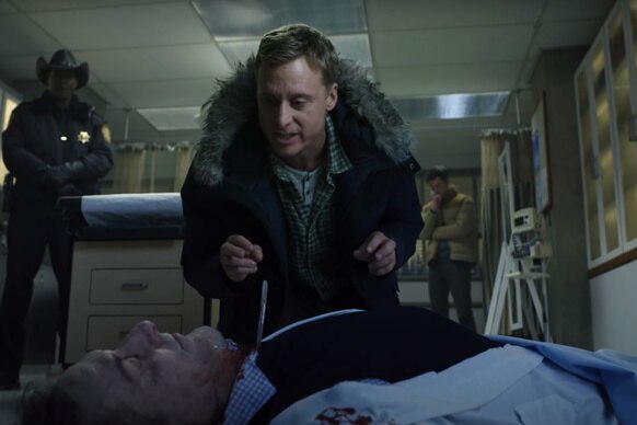 Harry (Alan Tudyk) stands over the dead body of Dr. Sam Hodges, M.D. (Jan Bos) in Resident Alien Season 1.