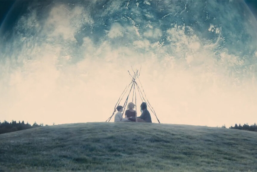 Three kids sit in a field in a tent made of sticks in Melancholia (2011).