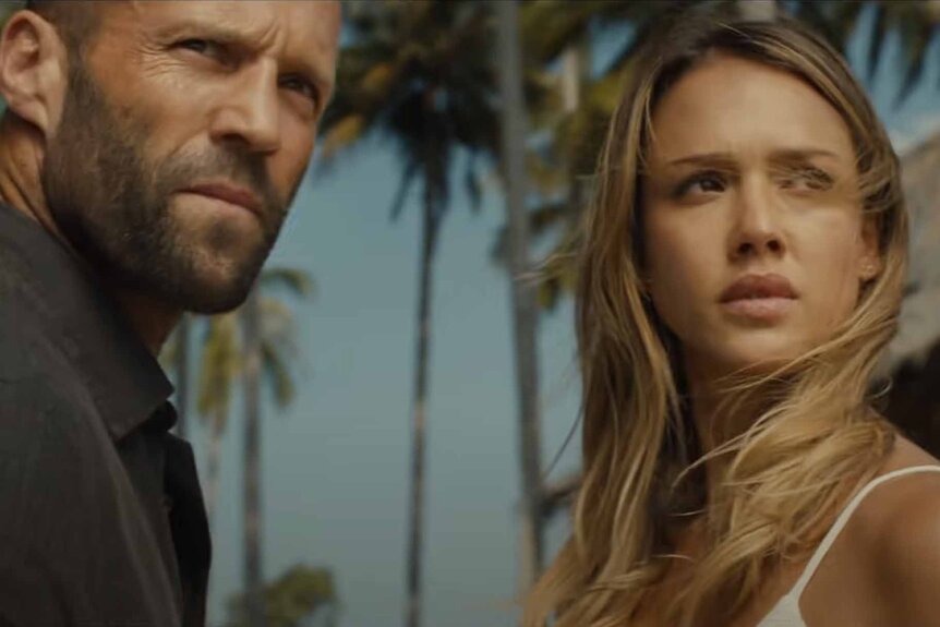 Arthur Bishop (Jason Statham) and Gina (Jessica Alba) appear with palm trees in the background in Mechanic: Resurrection (2016).