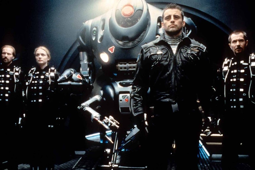 Gary Oldman, William Hurt, Heather Graham and Matt LeBlanc stand with a space machine in Lost In Space (1998)