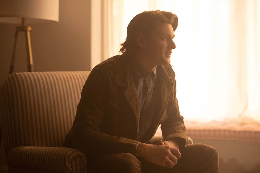 Warden Oliver (Luke Power) sits in a golden hour living room in SurrealEstate 203.