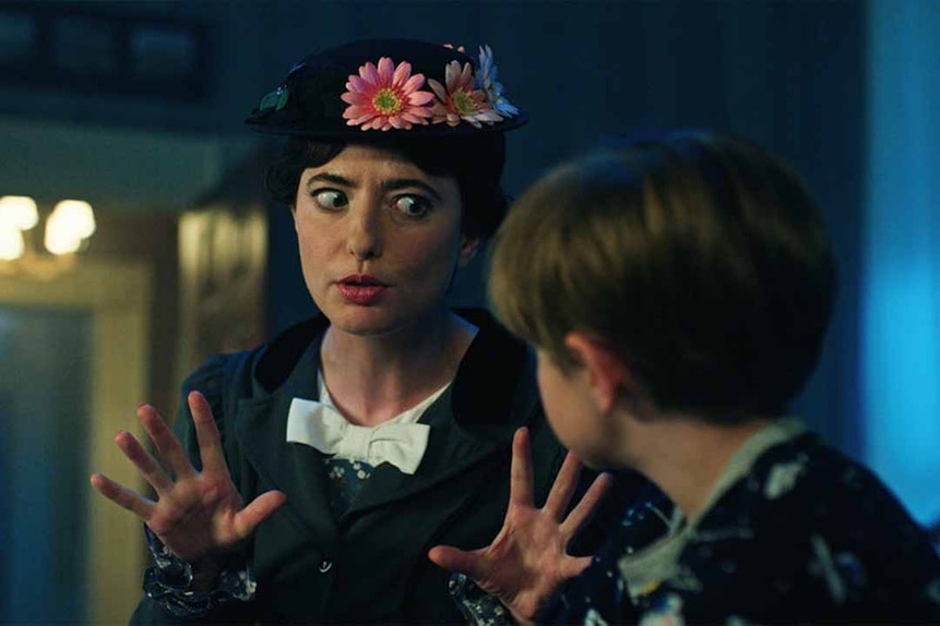 Annie Gilpin (Sarah Sherman) wears a flower hat and uses her hands to speak to a child in Chucky Season 3 Episode 4.