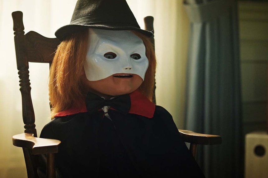 Chucky sits in a chair while wearing a while face mask and a hat in Chucky 304