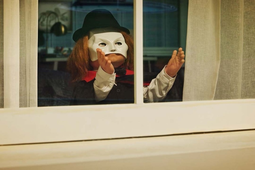 Chucky appears in a window wearing a hat and white mask in Chucky 304.