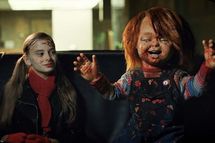 Caroline Cross (Carina Battrick) with blood on her face smiles in a car at a bloody Chucky in Chucky 303.