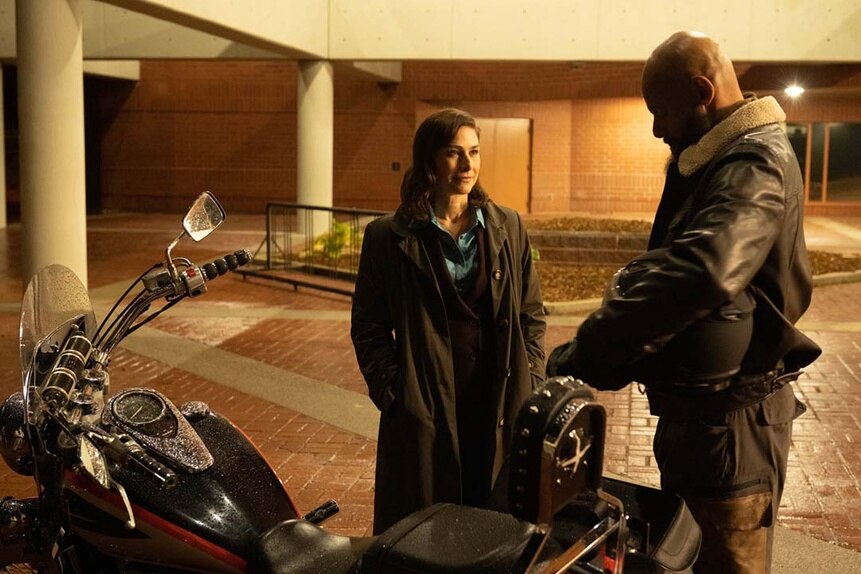 (l-r) Rochelle (Joy Tanner) talks to August Ripley (Maurice Dean Wint) as he holds a helmet near his motorcycle in SurrealEstate 205.