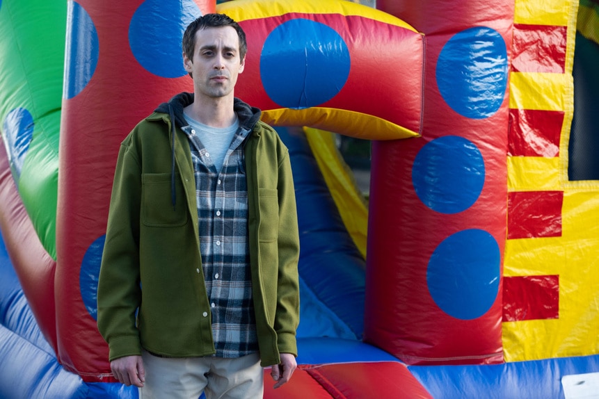 Alvin (Michael Rhodri-Smith) stands near inflatables in SurrealEstate 206.