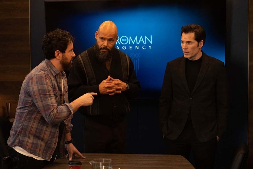 (l-r) Father Phil Orley (Adam Korson), August Ripley (Maurice Dean Wint), and Luke Roman (Tim Rozon) appear in front of a Roman Agency sign in SurrealEstate 207