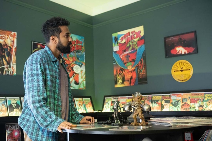 Zayan (Varun Saranga) rests against a table in a comic book store in SurrealEstate 209.