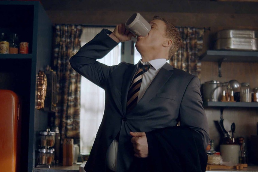Harry Vanderspeigle wears a suit and chugs from a mug in Resident Alien Episode 301.