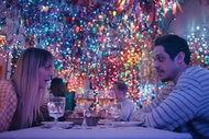 Kaley Cuoco and Pete Davidson sit at a table in a restaurant decorated with Christmas lights.
