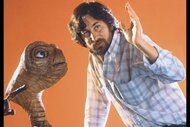 Director Steven Spielberg poses with E.T. at Carlo Rimbaldi studio in front of an orange background.