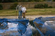 A couple looks down into a pool covered in leaves and blue tarp in Night Swim (2023).