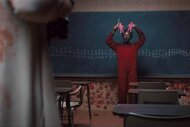 Red (Lupita Nyong'o) holds up red paper cutouts in front of a chalkboard with stick figures and red handprints under in Us (2019).