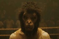 A monkey with the body of a man wears a yellow shirt in Monkey Man (2024).