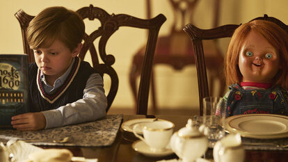 Chucky sits at a dining table with Henry Collins (Callum Vinson) in Chucky 301.