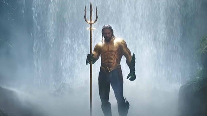 Aquaman (Jason Momoa) emerges from a waterfall holding a golden trident in Aquaman (2018).