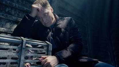 Harry Vanderspeigle rests on a cage holding Baby Alien within on Resident Alien Episode 308.