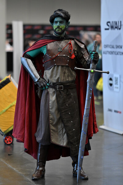A caped and armored cosplayer with green skin poses with a large sword during New York Comic Con 2023 - Day 1 at Javits Center.
