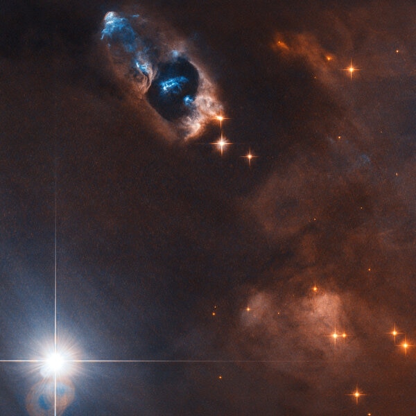 Young stars in the nebula NGC 1333 blast out twin beams of matter, creating eerie blue glows in this Hubble image. Credit: ESA/Hubble & NASA, K. Stapelfeldt; CC BY 4.0